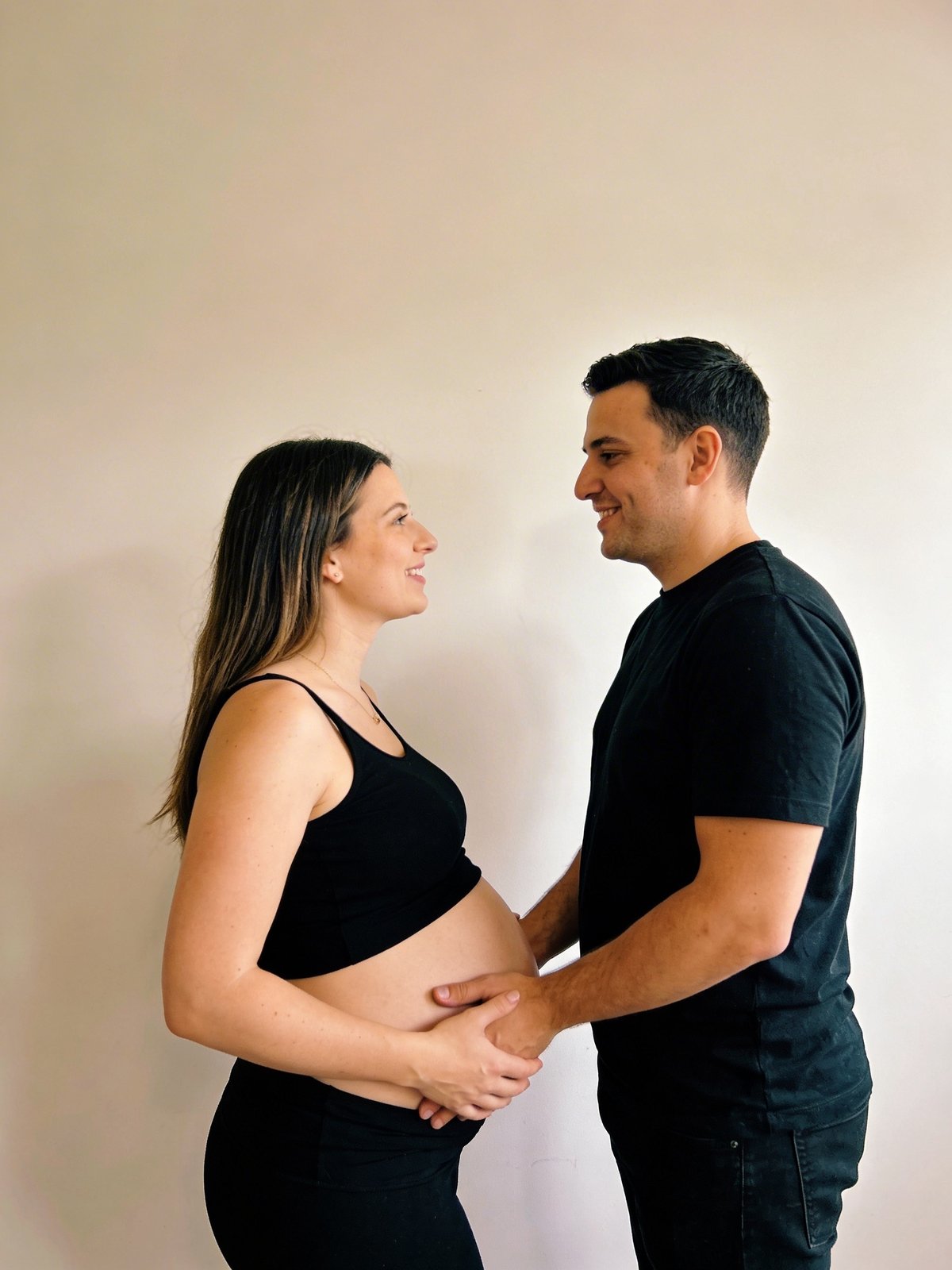 Expectant couple in coordinated outfits, face to face with hands resting gently on the bump