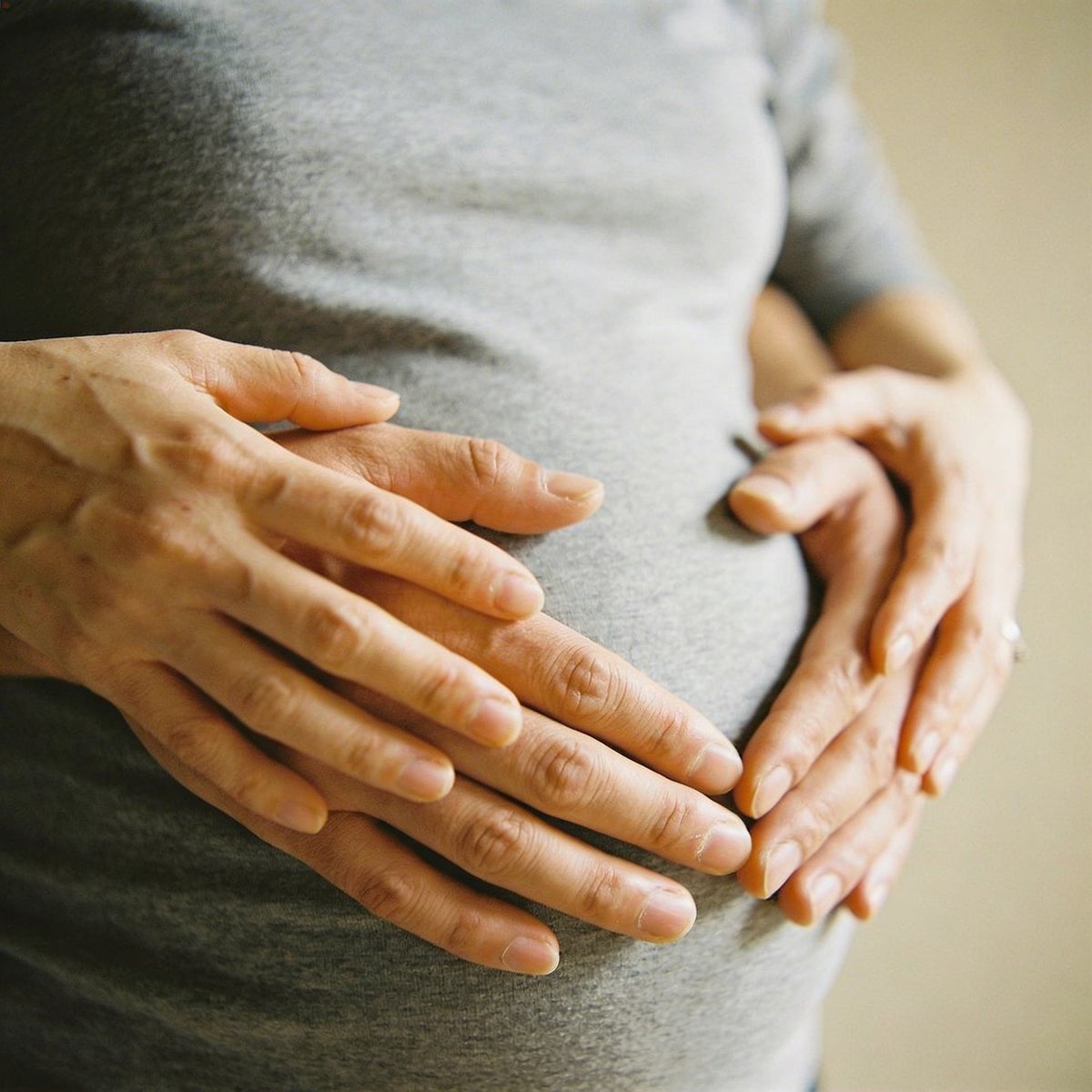 Close-up of mother and partner's hands forming a heart shape over the rounded bump